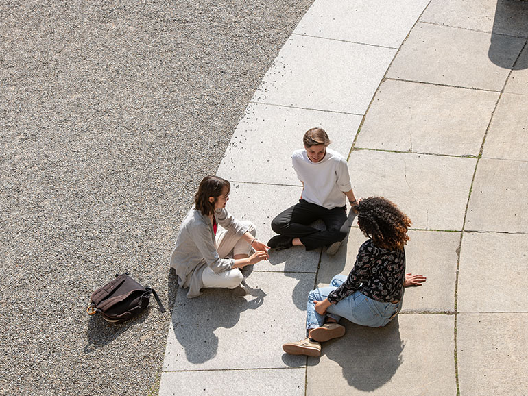 Studierende sitzen auf dem Boden vor dem Hauptgebäude